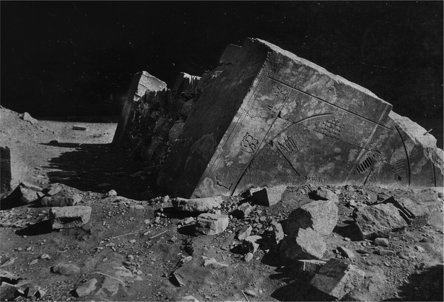 Black and white photo with film grain depicting the ruins of a stone structure with chiseled glyphs on the surface of a planet at night.